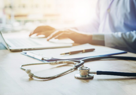 Doctor Typing Information On Laptop In Hospital Office Focus On Stethoscope